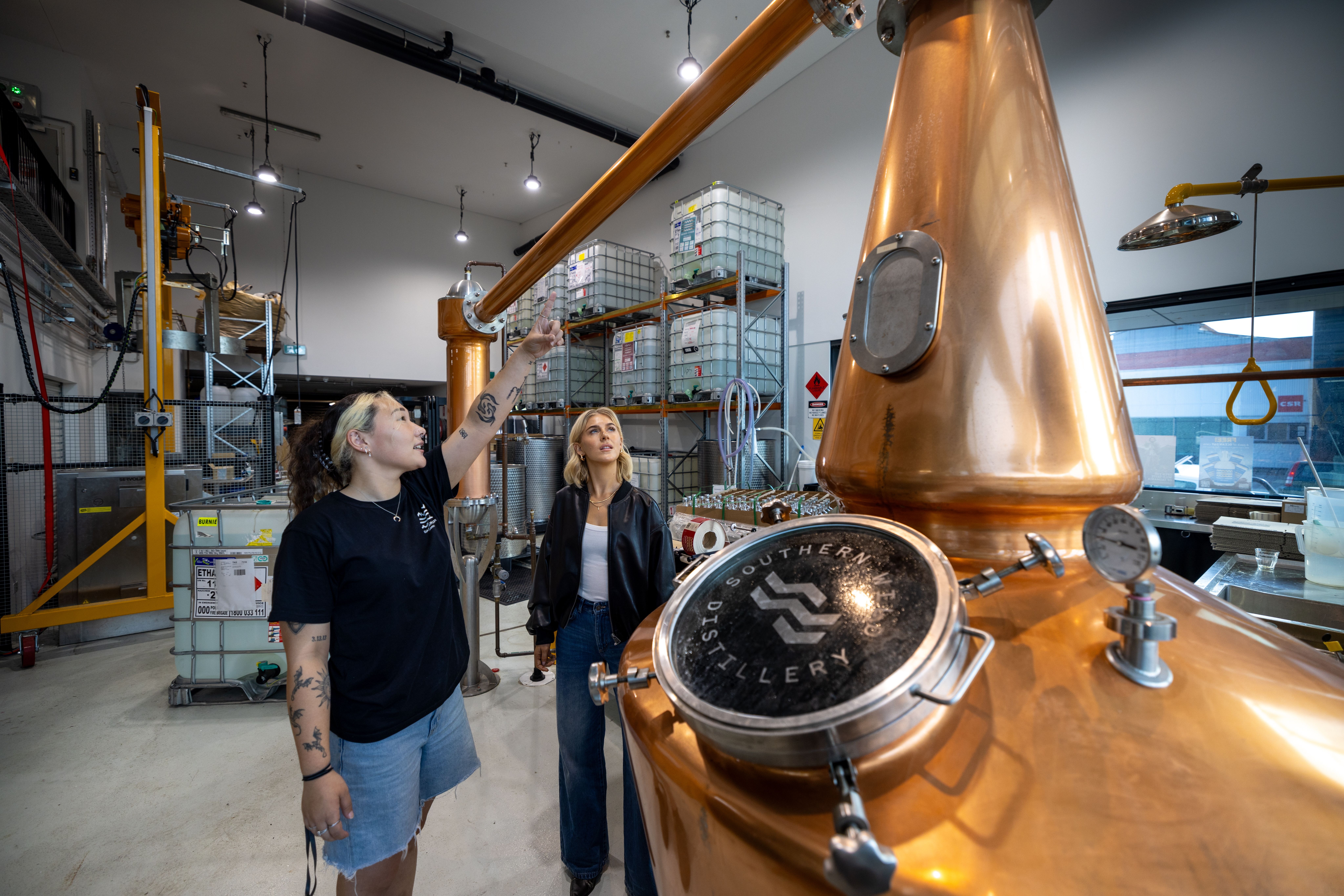 Two women at a copper still in a distillery